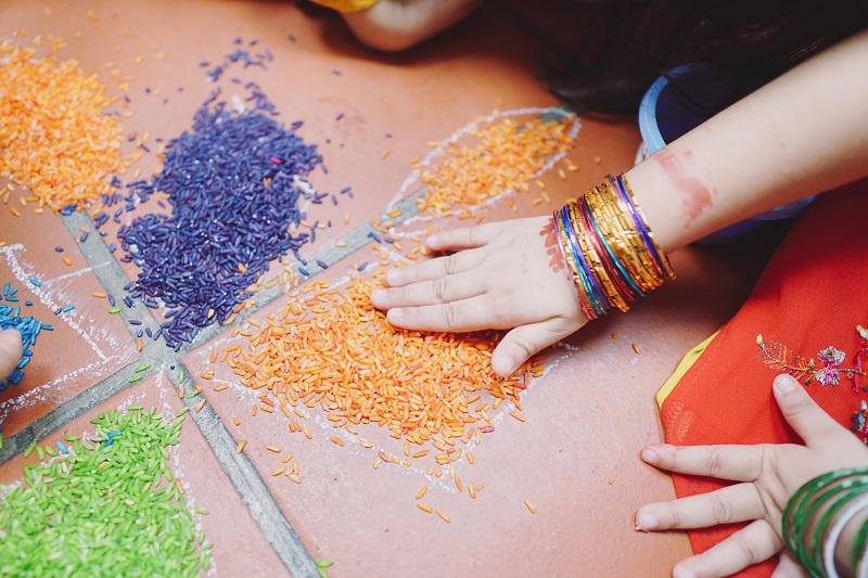 Children's hands working on creating a pattern using different coloured rice