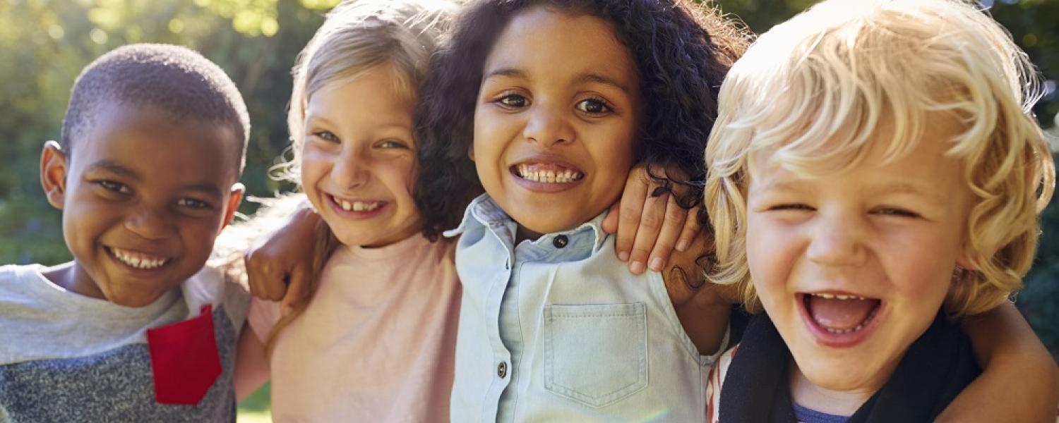 Four children in the garden, arms around each other and looking at the camera with joyful expressions