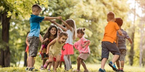 Two children making a bridge with their arms with other children running through underneath the arch 