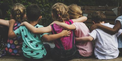 Children sitting in a row with their backs facing the camera and with arms wrapped around each other