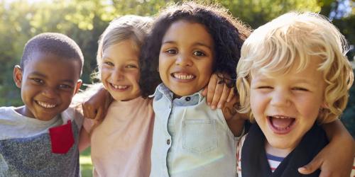 Four children in the garden, arms around each other and looking at the camera with joyful expressions