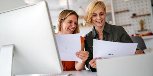 Two educators enthusiastically working in front of a laptop and and sheets of paper