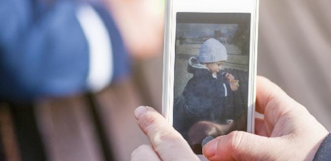 Person holding a mobile phone and taking a picture of a child sitting at a table