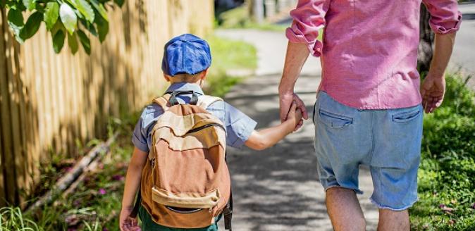 School aged child wearing a backpack, walking to school with an adult