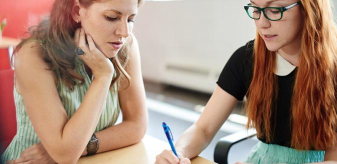 Two educators sitting at a desk in discussion and taking notes