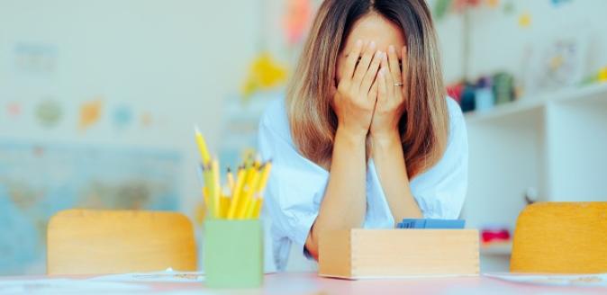 Distressed educator holding their face in their hands and covering their eyes