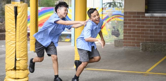 Two school aged children running and laughing in a school yard