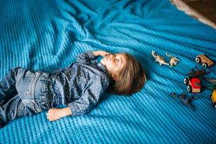 A child lying down on a blanket with eyes open, looking away from the camera