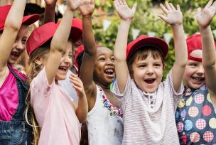 School-aged children wearing red baseball caps, celebrating with hands up in the air