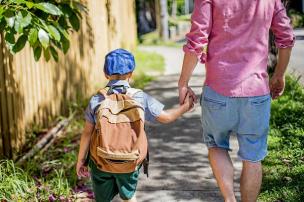 School aged child wearing a backpack, walking to school with an adult