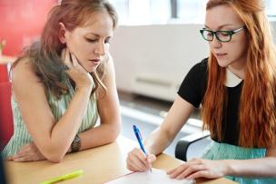 Two educators sitting at a desk in discussion and taking notes