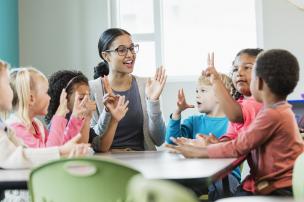 Educator sitting at a table with children playing a counting game with hands up in the air