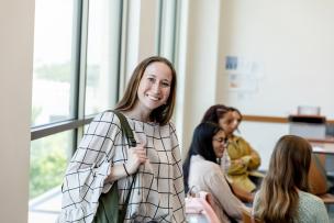 Educator facing the camera and smiling, with educators seated at a table behind her