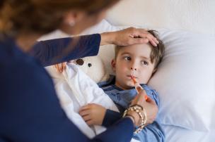 A child in bed with their soft toy and getting their temperature checked orally and with an adult's hand checking the child's forehead
